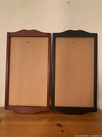 Front view of two Lang wooden calendar frames side by side on a wooden surface, showing the vintage red frame on the left and navy blue frame on the right, both empty.