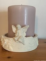 Porcelain candle holder displaying detailed fairy figure and nature motifs holding a lavender pillar candle.