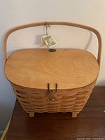 Front view of large wooden Peterboro footed basket with swing handle and closed hinged lid, showing latch and tag.