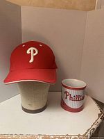 Both red Phillies baseball hat and 15 oz Phillies mug displayed together on table.