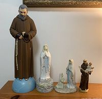 All four religious figurines arranged in a row: Padre Pio, musical Virgin Mary, praying Virgin Mary, Saint Anthony.