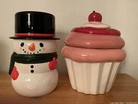 Snowman and cupcake ceramic cookie jars side by side showing overall appearance and size.