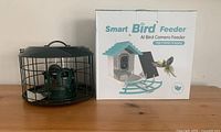 Smart bird feeder with protective cage and box featuring product name and image on the front.