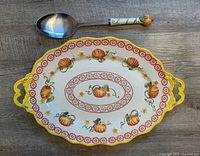 Top view showing oval platter with pumpkin and floral designs and matching serving spoon above it.