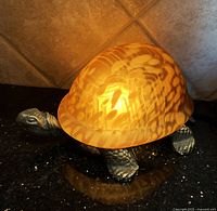 Side angle of turtle light showing amber stained glass shell and textured metal body.