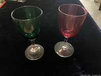 Two Victorian hand blown Bristol glasses, one green and one cranberry, displayed on a black surface.
