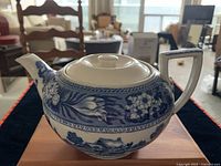 Front side of the blue and white teapot showing floral patterns on the upper half and white lid on top.