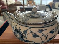 Side view of the blue and white porcelain teapot showing the floral decoration and metal handle with decorative ends.