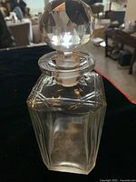 Close-up image of a clear Val Saint Lambert crystal decanter with faceted crystal stopper showing geometric cut designs on the glass body.