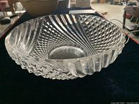 Clear crystal bowl with diamond cut and scalloped edge design, placed on dark fabric to highlight details.