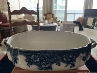 Blue and white porcelain floral serving dish with scalloped edges and side handles, shown on table with a blurred room background.