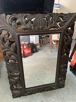 Full view of the rectangular mirror showing its carved wooden frame with intricate floral and shell pattern designs in dark brown.