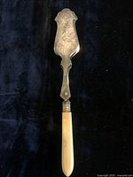 Full view of silver plated serving tong showing engraved decorative blade and mother of pearl handle.