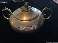 Silver sugar bowl with lid, showing overall shape, handles, and surface condition.