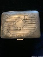 Top view of the rectangular silver cigarette case showing detailed etched design and engraved central motif