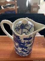 Front angled view of the rectangular-shaped syrup pitcher with lid, showing the blue and white oriental pattern and handle.