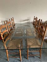 Photo shows the rectangular glass dining table with chrome legs and six wooden chairs with cane seats around it