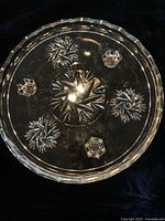 Top down view showing clear glass plate with embossed floral and geometric patterns and scalloped edge.
