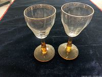 Pair of vintage crystal glasses with amber stems and gold floral rim pattern shown on a dark cloth.