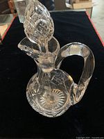Full view of vintage clear glass decanter with stopper showing cut glass patterns and curved handle.