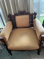 Front view showing gold patterned upholstery and carved wooden frame of the vintage armchair