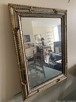 Angled view of the rectangular wall mirror showing the gold wood frame and reflection of a furnished room.