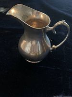 Side angle photo of the vintage pewter pitcher showing its bulbous shape, curved handle with thumb rest, and wide spout.