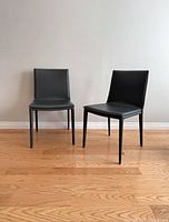 Two Nuevo Palma leather dining chairs in matte dark grey shown side by side on a hardwood floor against a plain wall.