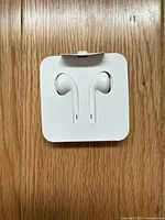 Apple EarPods neatly packed in original square cardboard case, showing the earbuds and cable.