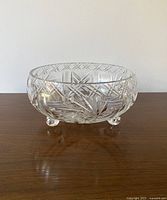 Side view showing the cut patterns and three rounded feet of the crystal bowl on wooden surface against a plain white background.