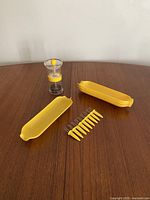 Four yellow corn dishes, eight yellow corn holders, and salt and pepper grinder arranged on a wooden surface.