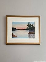 Frontal view of the framed landscape painting depicting a lakeside scene with trees and sunset sky.