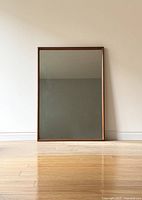 Full front view of rectangular teak mirror leaning against wall