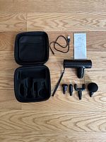 Full lot display showing fascial gun, carrying case, USB cable, five massage heads, and manual on wooden floor.