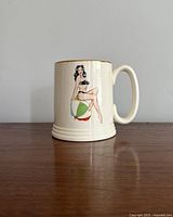 Side view showing pin-up style woman sitting on a striped beach ball, black bikini, gold rim detail on mug