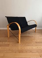 Angled side view showing the curved bentwood armrests, frame, and two black cushions on the sofa with one cushion missing.