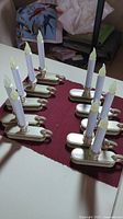 Photo showing all 10 electric window candles arranged on a red cloth on a white table. Candles have gold bases and white candle bodies with flame-shaped tips.