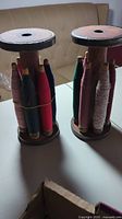 Front view of two antique wooden thread spool holders with multicolored thread spools.