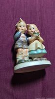 Front view of porcelain Hummel figurine showing boy and girl children standing side by side, detailed ceramic paint and facial features.