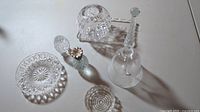 Seven-piece set of cut glass crystal decor items arranged on a flat surface, displaying diverse shapes and intricate cut patterns, including a basket, bell, dishes, and perfume bottle.
