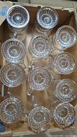 Top-down view of 12 clear glass footed mugs arranged in a box, showing starburst pattern on the base.