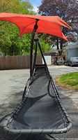Front view of black mesh fabric hammock with metal frame and attached red sun shade outdoors.
