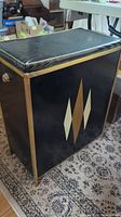 Side view of black hamper with gold diamond geometric design and vinyl cushioned lid.