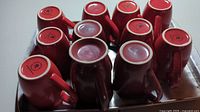 View of the bottoms of the 11 ceramic mugs showing red and maroon colors and manufacturer marks.