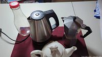 Full lot as seen from above on red cloth, showing electric kettle, Moka pot, glass bottle, and ceramic teapot.
