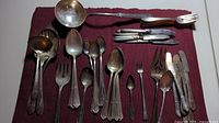 Full set of assorted silver-plated silverware on burgundy cloth showing spoons, forks, knives, ladles and serving utensils