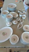 Complete view of dinnerware pieces arranged on table showing plates, bowls, cups, saucers and creamer/sugar bowl with pink orchid floral design