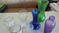 Top view of the 8 glass vases arranged on a table showing colors and textures including green ribbed, blue smooth, purple hobnail and clear glass vases.