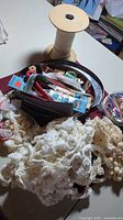 Photo showing metal tin filled with various sewing supplies including large spool of white elastic, multiple lace trims, and assorted sewing notions.
