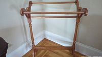 Full image of traditional brown wooden quilt stand with three horizontal rails and turned wood supports.
